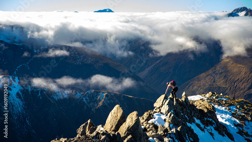 Brave hiker girl scrambles along very narrow rocky ridge on way to Avalanche Peak summit. Breathtaking mountain views in Arthur's Pass National Park, Canterbury, South Island, New Zealand.