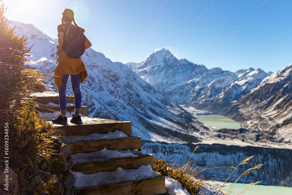 Naklejka premium Hiker girl climbs snow-covered stairs on Sealy Tarns Track, admiring alpine views of Aoraki Mount Cook and surrounding glacial lakes, South Island, New Zealand