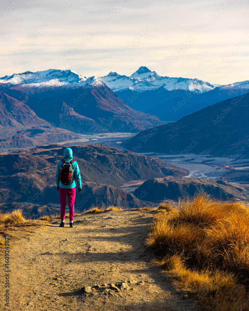 Fototapeta premium Hiker girl hikes along Roys Peak trail and admires stunning panoramic views over Lake Wanaka and surrounding alpine peaks near Wanaka, Otago, South Island, New Zealand.