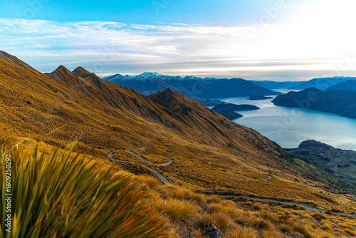 Stunning panoramic sunrise view from Roys Peak summit overlooking Lake Wanaka and surrounding snow covered peaks near Wanaka, Otago, South Island, New Zealand