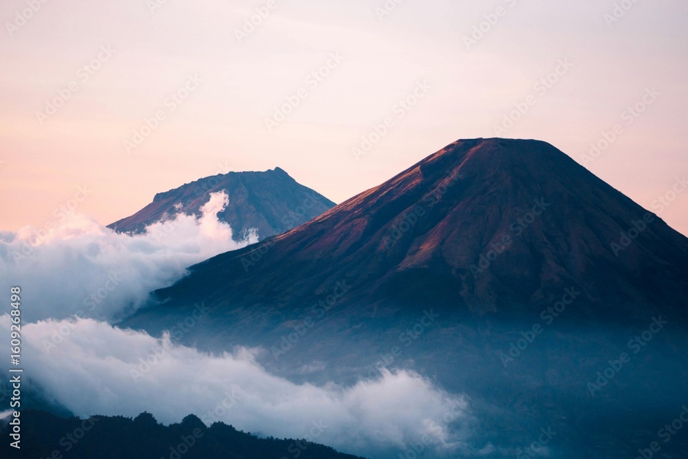 Fototapeta premium Volcanoes Surrounded by Clouds Under a Pastel Sky at Sunrise