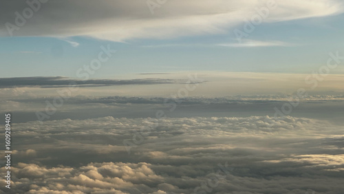 A breathtaking aerial view from above a sea of clouds during a beautiful golden hour. The sky is a soft blue, creating a serene and vast skyscape.