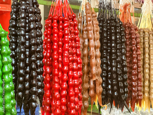 A colorful and appetizing display of traditional Georgian churchkhela sweets hanging in a market. The candle-shaped candies, made from nuts and thickened grape juice, are shown in various colors