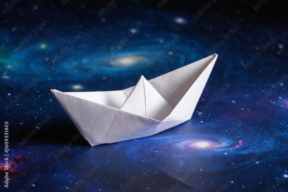 Obraz premium Serene White Origami Boat Sailing on a Cosmic Galaxy Background: Hope, Dreams, and Exploration Concept