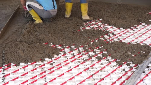 Workers pour concrete mortar onto the top of underfloor heating pipes during construction.