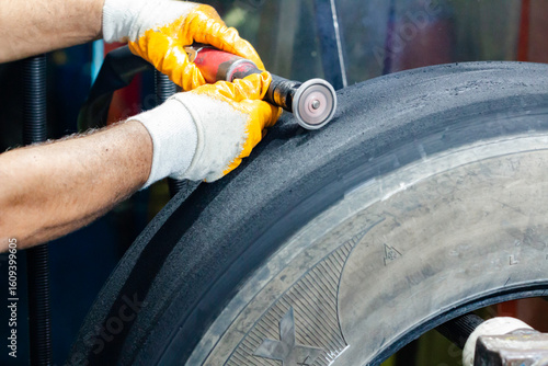 Tire retreading master cleans the wounds of the truck tire coming out of the rasping machine with a grinder.