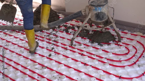 Workers pour concrete mortar onto the top of underfloor heating pipes during construction.