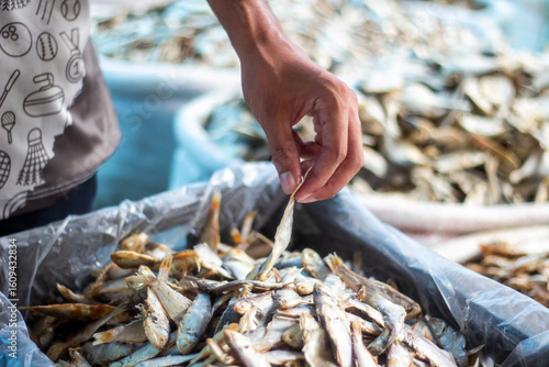 A man holds a dry fish on the sack in the market