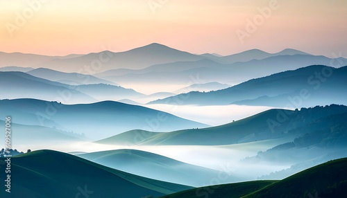 Misty mountain ranges meet a tranquil sunrise. Lush, rolling hills painted in shades of blue and green, are enveloped in a soft, hazy mist.  Sunrise paints the sky in pastel tones of peach and rose