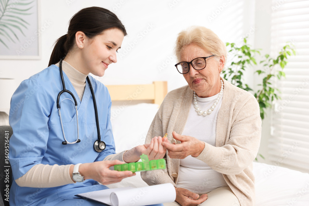 Fototapeta premium Nurse giving pills to senior woman indoors. Home health care service