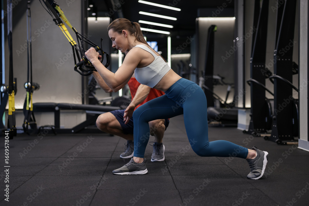 Obraz premium Young woman exercising with suspension trainers with professional personal coach in gym