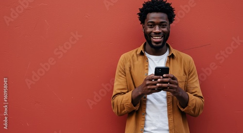 Happy Black Man Holding Phone with Red Wall Background Smiling