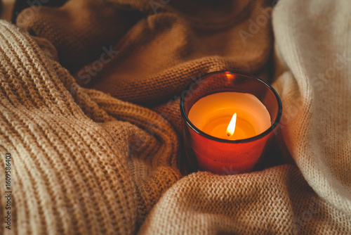 Schilderij op canvas Top view of a burning candle on cozy knitted blankets in warm beige and brown tones