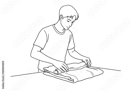 A young man carefully folds a piece of clothing on a flat surface, focused.