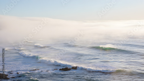 Gentle ocean waves crash on a misty shore under a soft sky