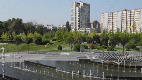 Dnipro, Ukraine. A beautiful park with fountains and trees against of tall houses, buildings and skyscrapers. Drone view, cityscape. Spring, summer street