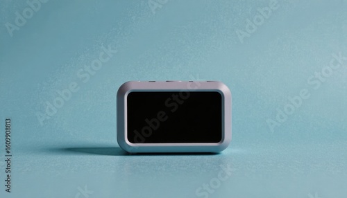 A contemporary digital smart clock with a minimalist grey casing and a blank screen, resting on a serene light blue surface for a modern, clean aesthetic.