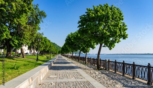 Riverfront promenade lined with lush greenery under a vibrant blue sky