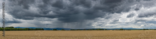Panoramansicht eines über das Land ziehenden Unwetters mit Starkregen und grauer-schwarzer Wolkendecke mit bestelltem Acker im Vordergrund