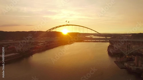 The sun sets behind a bridge over a river in portland, oregon