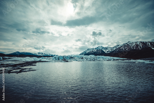 Glacial Lake with Snowy Mountains Under Cloudy Sky