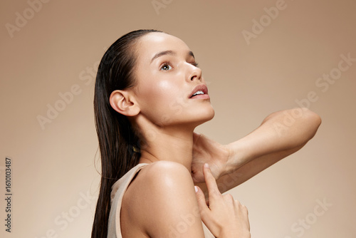 Portrait of a young woman with wet hair looking upwards, showcasing natural beauty and glowing skin against a soft, neutral background