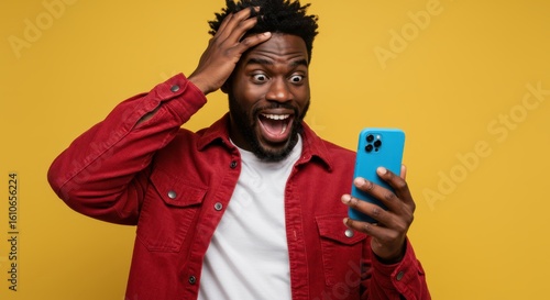 A black man with a beard and curly hair reacts with shock and excitement while looking at his smartphone, holding his head in disbelief against a vibrant yellow background