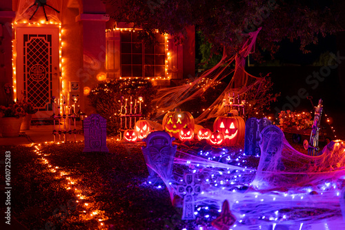 Glowing outdoor decorations with pumpkins, tombstones and orange and purple garlands on the house porch