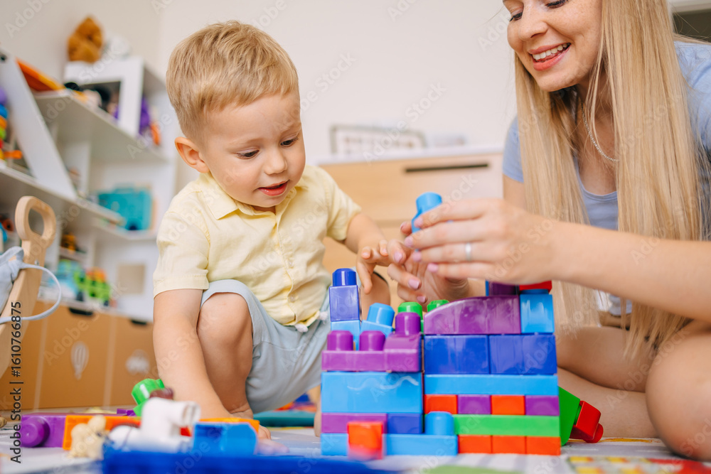 Fototapeta premium Mother and child building with colorful blocks in a playroom
