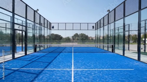 Padel Court with Blue Surface and Glass Walls, Empty and Ready for a Match, Modern Outdoor Padel Tennis Court on a Clear Sunny Day