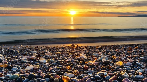 Golden Sunset Embrace on Coastal Shore: Witness the serene convergence of the sun's golden rays with the tranquil sea at twilight, where the stony shore whispers tales of time and the elements.