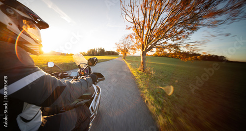 Driver riding motorcycle on empty road during sunset , view from the passenger side