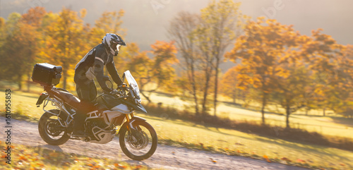 Driver riding motorcycle on empty road during sunset, autumn mountains