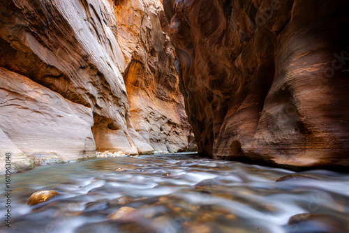 Narrow canyon walls with a flowing river in Zion National Park, USA, showcasing unique sandstone formations and smooth water.