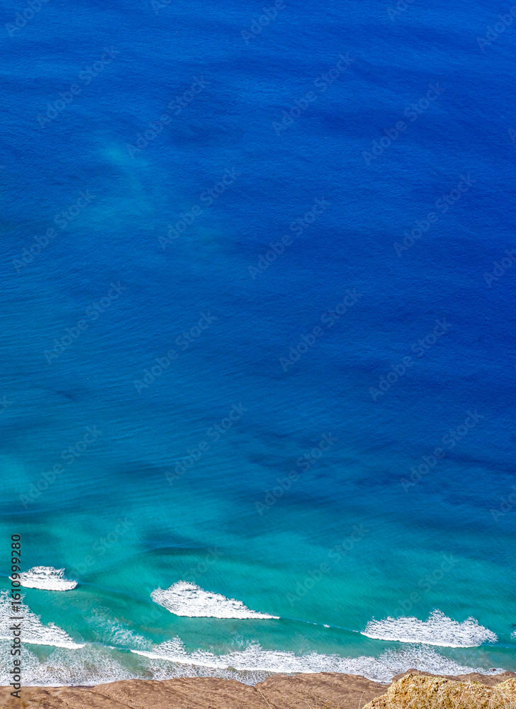 Obraz premium Blue ocean with waves and a sandy beach, top view.