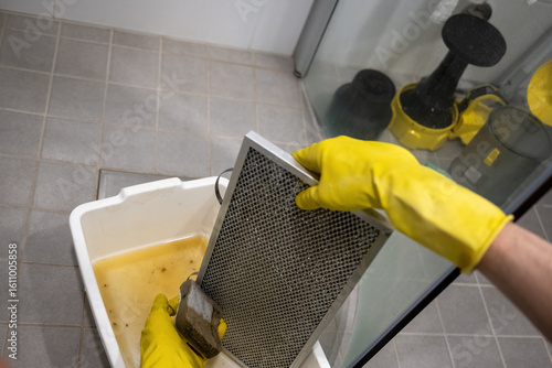 Tableau sur toile Person cleaning greasy metal range hood filter with sponge and rubber gloves ove