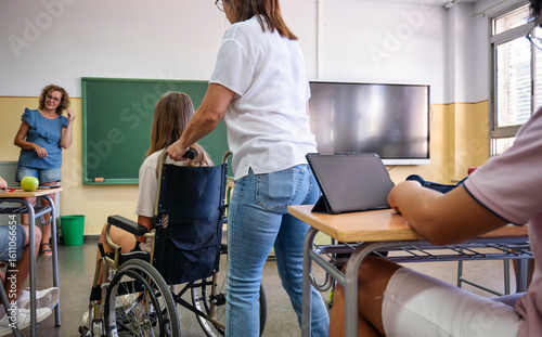 Teacher assisting a student in a wheelchair during inclusive classroom activity with tablets and diverse participation