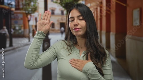 Wallpaper Mural Woman pledging outdoors on a street with a focused expression, hand raised and dressed casually, highlighting her youthful hispanic features and serene city vibe. Torontodigital.ca