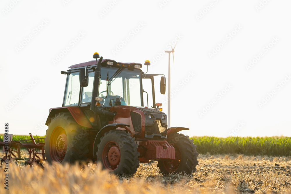 Fototapeta premium Agricultural tractor on the field with wind turbines