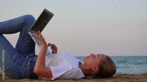 A girl with a laptop lies near the sea and works on the computer. Working with a laptop near the sea.