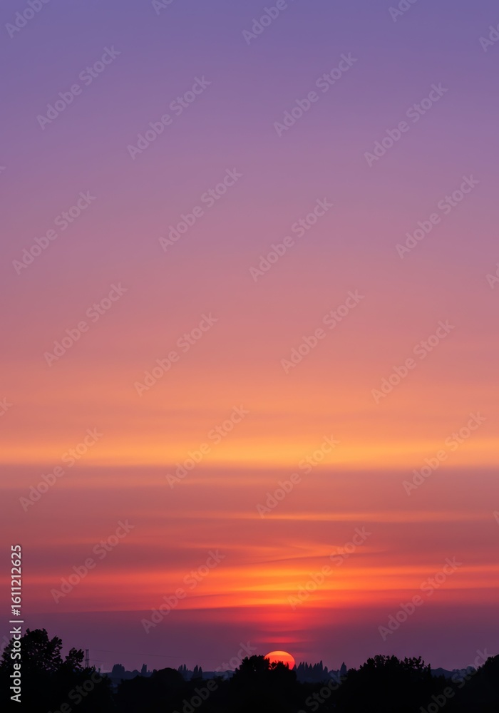 Fototapeta premium Vivid Sunset Sky with Orange and Purple Colors Over Silhouetted Trees