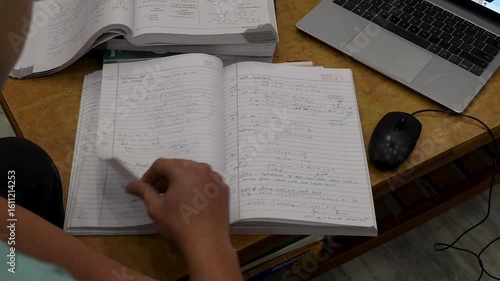 Indian student studying from notes with laptop and textbooks at home