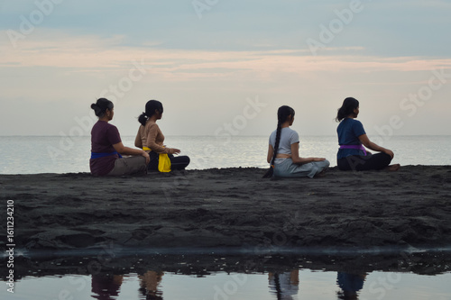 Sitting in silence with closed eyes and relaxed hands on their thighs, the girls immerse in a deep meditative state as part of their calming morning beach ritual.