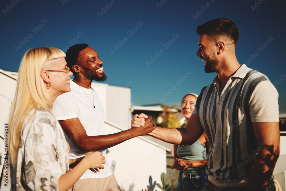 Obraz premium Group of cheerful multiracial friends greeting each other shaking hands during a rooftop party