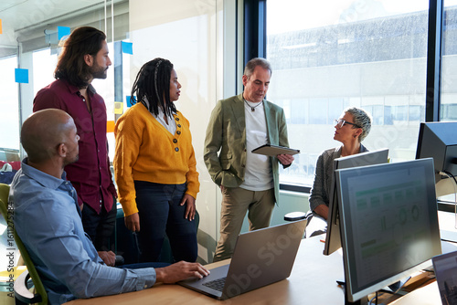 Business colleagues discussing project strategy in modern office, using digital tablet and laptop for analysis and planning. Image with copy space.