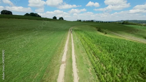 FPV drone orbiting around a cyclist riding on a country road through green hills and fields