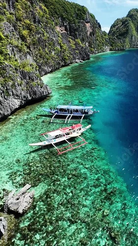 Aerial view of boats and coral reef along limestone cliffs in El Nido, Palawan. Traditional boats floating near coral reef and cliffs in El Nido, Palawan, Philippines, vertical screen