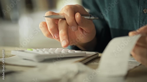 A person is actively calculating expenses using a calculator while sorting through a stack of receipts. This focused budgeting session takes place in a cozy home environment