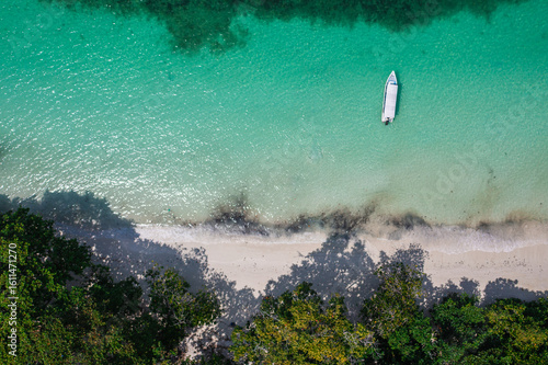 A stunning aerial view of a serene tropical coastline featuring a small white boat anchored in crystal-clear turquoise waters near a secluded sandy beach.