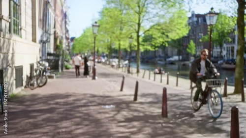 Wallpaper Mural Defocused scene captures a man and woman walking beside amsterdam canals with lush trees, bicycles, and historic buildings, embodying the essence of a vibrant, urban landscape. Torontodigital.ca
